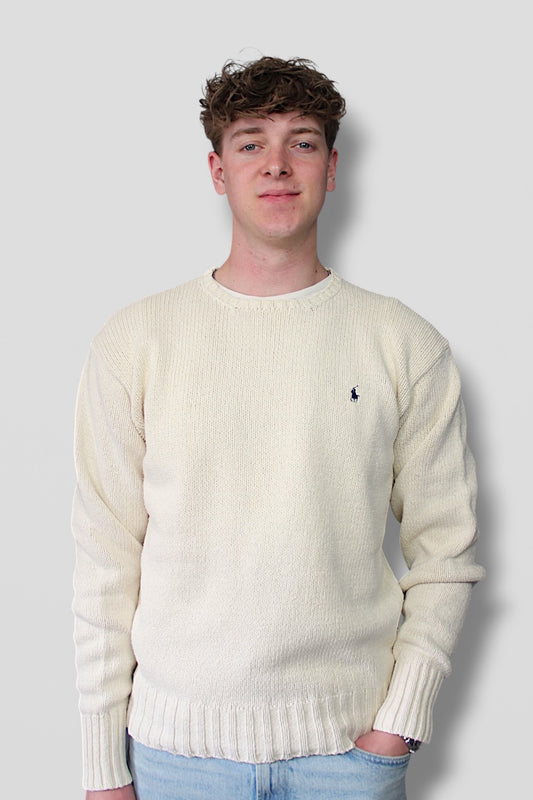Man wearing a cream sweater with a small logo on a plain background