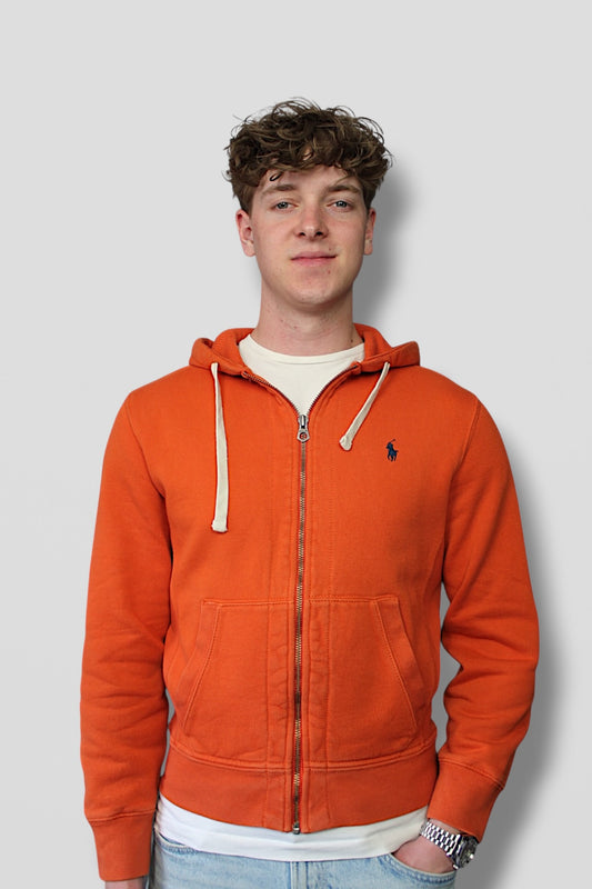 Person wearing an orange hoodie with a visible brand logo on a plain background